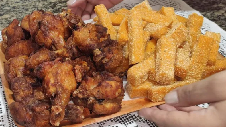 Golden crispy fried polenta slices served alongside crispy fried chicken wings on a rustic wooden platter, garnished with fresh parsley.