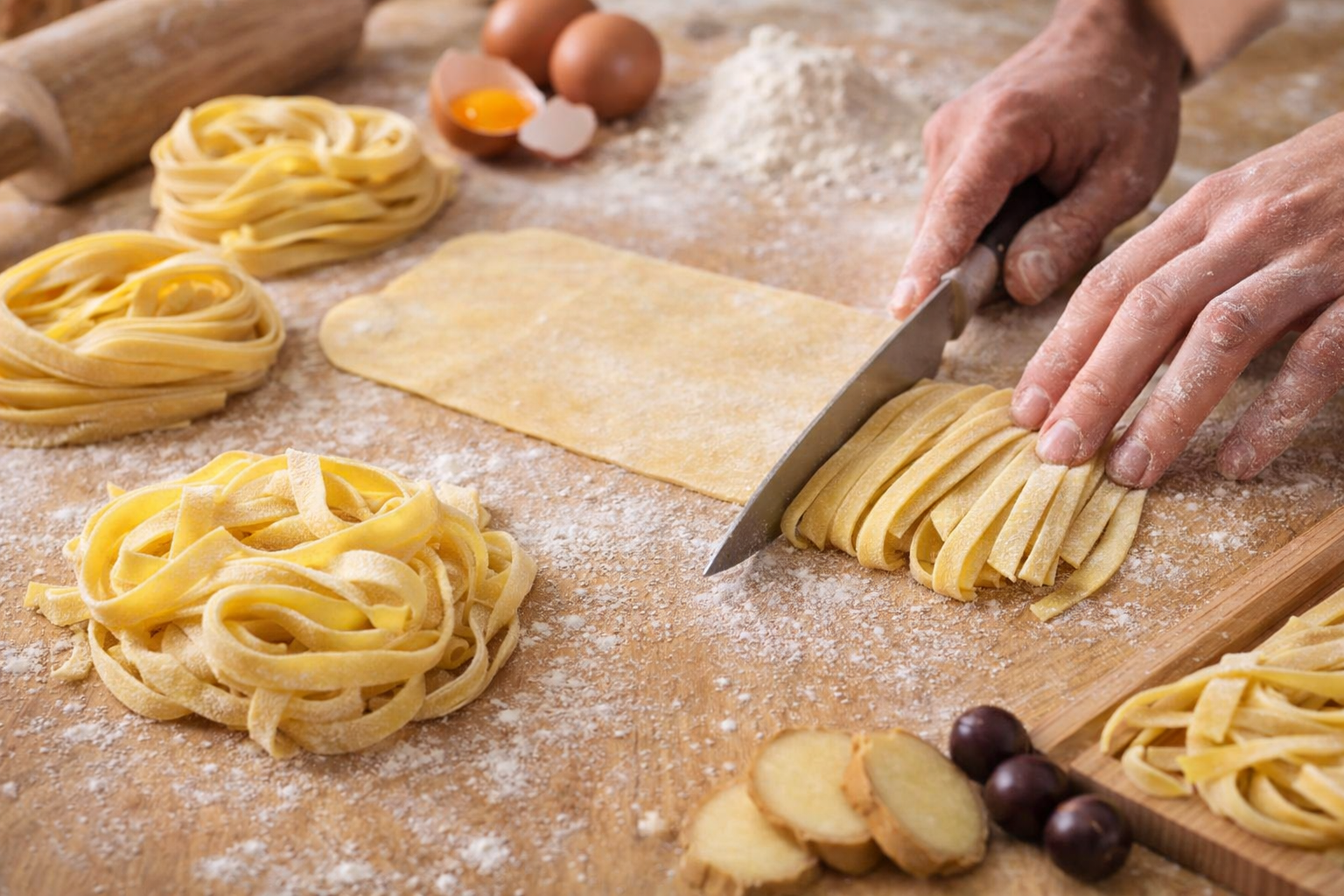 The artisanal process of preparing tagliatelle: hands cutting the fresh pasta on a floured surface, with a rolling pin, eggs, and flour in the background. The warm lighting enhances the golden hue of the pasta and conveys the welcoming feeling of an Italian kitchen.