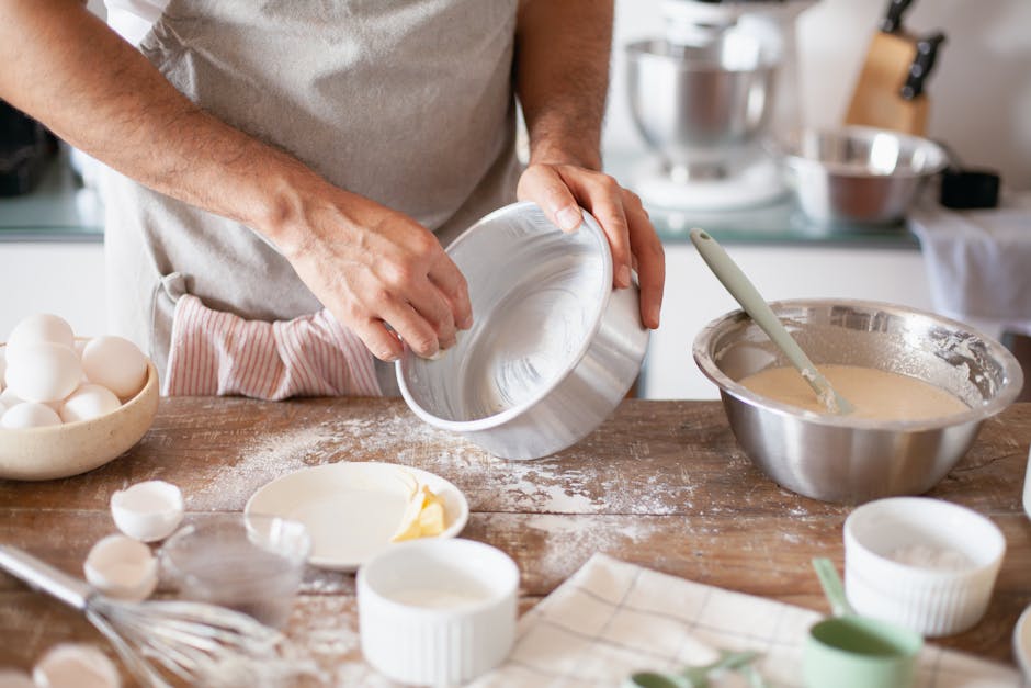 Close-up of hands greasing a pan with ingredients ready for baking in a kitchen.